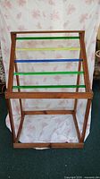 Front view of handmade wooden rack with four colored acrylic dowels (green, blue, green, yellow-green). Natural wood finish frame, designed for storage or display.