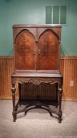 Closed view of vintage wood media cabinet with carved details and arched double doors.