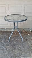 Full view of the round outdoor metal and glass table on concrete surface.