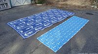 Large and medium anchor pattern rugs laid flat on asphalt ground showing top sides