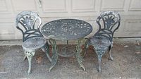 Full view of the set showing two floral design metal chairs and round table with rusting and fading visible