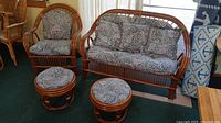 Set of 4 wicker furniture pieces including a couch, armchair and two footstools with patterned cushions in muted paisley design.