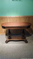 Front view of wooden table showing rounded rectangular top, carved double pedestal support base mounted on flat stretcher.