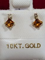 Front view photo of 10KT gold earrings with citrine and diamond stones on white earring holder.