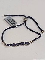 Top view showing five oval blue iolite stones set in silver prongs with dark blue braided adjustable cord and silver-tone end caps and slider bead.