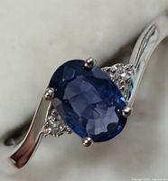 Close-up front view of 10KT white gold ring featuring an oval blue sapphire with diamond accents