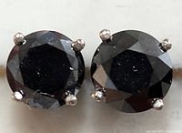 Close-up front view of two round black diamonds in four-prong gold settings.