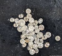 Close up image of loose round diamonds on black textured surface showing several stones in varying sizes.