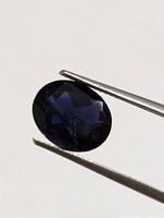 Close-up view of oval faceted deep blue violet iolite gemstone held in tweezers