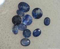 Close-up image of eleven loose faceted blue sapphires on a light surface showing their shapes, color and clarity.