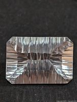 Front view showing the rectangular emerald cut and striated facets reflecting light within the clear white topaz gemstone.