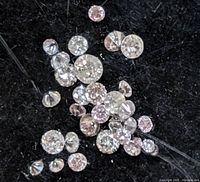 Close-up photo showing multiple loose natural fancy pink and colorless round cut diamonds scattered on a black fabric background.