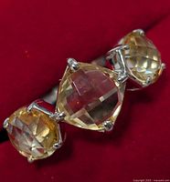 Close-up photo of the front of silver ring with three faceted citrine stones set in prongs against a red background.