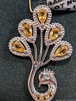 Front view of the silver peacock pendant showing the five citrine stones and detailed silver work around each stone. The pendant is shaped with a curled peacock body and feathers extended upwards.