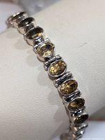 Close-up angled photo of the sterling silver bracelet with oval citrine gemstones on a white display stand.