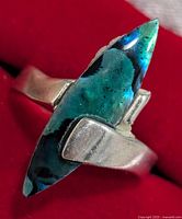 Close-up view of sterling silver ring with marquise-shaped, multi-colored blue-green gemstone on red background.