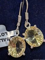 Close-up photo showing silver drop earrings with oval lemon quartz gemstones secured in four-prong settings, showing facets and clarity of the stones, hooked silver wire fastening with coiled design.