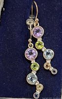 Pair of silver drop earrings featuring multiple round gemstones of purple, green, blue, yellow, and dark blue colors set in bezel mounts on a hook wire.