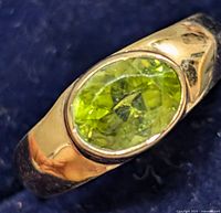 Close-up of oval peridot gemstone set in a silver ring band, showing facets of the stone and reflective surface of the silver.