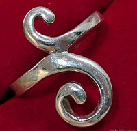 Close-up photo showing silver ring's curled swirl design from one angle on red background