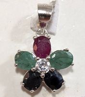 Silver flower-shaped pendant with five gemstones: ruby, emeralds, sapphires, and a central clear stone.