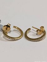 Pair of gold-tone small hoop earrings laid on white background showing white topaz stones along the outer edge with post-back closures