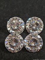Four loose round brilliant cut colorless moissanite gemstones on black background
