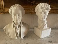 Photo showing both plaster busts placed side-by-side on a marble surface with a painting behind