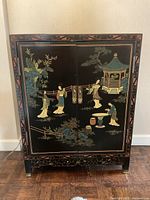 Full front view of black lacquer cabinet with painted scene and brass hardware