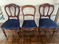 Front view of three antique wooden chairs with upholstered blue seats placed side by side showing design differences and wood finish.
