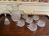 Full set on wooden surface including pitcher, six cups, and bell.