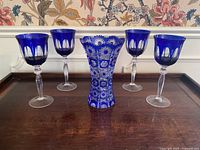 Front view of cobalt blue cut-to-clear crystal vase and four matching wine glasses on wooden surface