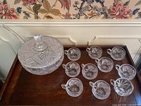 Photo showing crystal punch bowl with lid, 10 matching handle cups and ladle on a wooden surface.