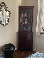 Full view of dark wood curio cabinet positioned in corner between mirror and window.