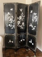 Full view of the three-panel black folding screen with white floral and bird relief designs on black lacquer background, showing the overall condition and style.