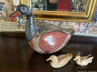 Photo showing three wooden duck figurines: one large painted duck with visible repair and two smaller natural-finish ducks.