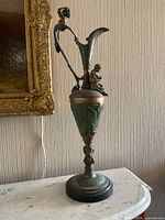 Front view of the antique metal figurine ewer showing the main human figure handle, spout and seated child figure on the side.