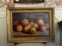 Full view of framed oil painting depicting apples in front of a wicker basket.