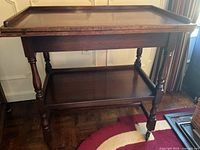 Front-right angled view of the wooden games table showing the raised edges, turned legs, lower shelf, and caster wheels.