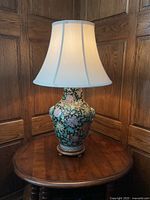 Front view of ceramic table lamp showing detailed floral design and white fabric bell-shaped lampshade.
