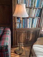 Full lamp standing beside a bookshelf and plaid sofa, showing complete lamp and lampshade.