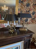 Overview of both brass bouillotte lamps on sideboard against floral wallpaper