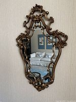 Front view showing full ornate carved frame and mirror surface reflecting living room furniture and wall art.