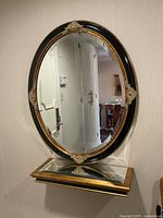 Front view of the oval mirror showing black frame with gold trim and ornate gold decorative accents.