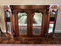Front view of the wooden cabinet showing three mirrored doors and corner panels with carved decorative trim.