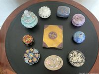 All nine assorted trinket boxes arranged on a round wooden table with a black center.