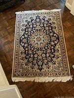 Full view of one rectangular rug with a complex medallion floral pattern in navy and cream colors placed on a wooden floor.