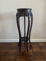 Front view of a tall, narrow wooden stand with a round marble top and carved floral designs.