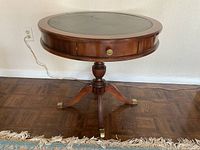 Front view of round wooden table showing leather top, drawer and tripod base with brass tips