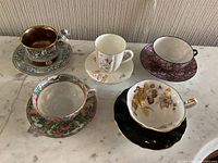 Five teacups with matching saucers displayed on a marble surface showing the top and inside of cups.